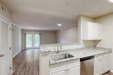 Located at 11 Ledgewood Rd in Groton, Connecticut, this one-bedroom, one-bathroom residence offers a well-designed single-floor layout with a thoughtful combination of comfort and functionality. The open-concept living, dining, and kitchen area serves as the heart of the home, featuring warm wood-look flooring, crown molding, and recessed lighting throughout. The kitchen is outfitted with white cabinetry, granite countertops, stainless steel appliances including a dishwasher and refrigerator, and a peninsula that provides additional prep space and a natural transition into the living area. French doors in the living room lead to a private balcony with green metal railings, offering pleasant views of mature trees and lush landscaping. The bedroom is generously proportioned, featuring plush carpeting, a large window with natural light, and access to multiple closets for ample storage. The full bathroom includes a double-sink white vanity, a large mirror, and wood-look flooring, providing a clean and functional space. Additional conveniences include an in-unit laundry area and a utility room. With neutral tones and modern finishes throughout, this residence presents a move-in-ready interior in a well-maintained setting.