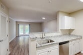 Located at 11 Ledgewood Rd in Groton, Connecticut, this one-bedroom, one-bathroom residence offers a well-designed single-floor layout with a thoughtful combination of comfort and functionality. The open-concept living, dining, and kitchen area serves as the heart of the home, featuring warm wood-look flooring, crown molding, and recessed lighting throughout. The kitchen is outfitted with white cabinetry, granite countertops, stainless steel appliances including a dishwasher and refrigerator, and a peninsula that provides additional prep space and a natural transition into the living area. French doors in the living room lead to a private balcony with green metal railings, offering pleasant views of mature trees and lush landscaping. The bedroom is generously proportioned, featuring plush carpeting, a large window with natural light, and access to multiple closets for ample storage. The full bathroom includes a double-sink white vanity, a large mirror, and wood-look flooring, providing a clean and functional space. Additional conveniences include an in-unit laundry area and a utility room. With neutral tones and modern finishes throughout, this residence presents a move-in-ready interior in a well-maintained setting.