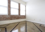This single-floor space showcases a thoughtfully designed open-concept layout that seamlessly connects the living area to the kitchen. One of the most distinctive features is the polished concrete flooring, accentuated by bold geometric dark inlay lines that add a striking artistic element to the space. The clean, neutral walls in a warm white tone create a bright and airy ambiance throughout.

The kitchen is a functional centerpiece, featuring stainless steel appliances, including a full-sized refrigerator, and a breakfast bar with elegant granite countertops. White cabinetry provides ample storage, while pendant lighting fixtures hang overhead, casting a warm, focused glow over the counter space. The kitchen opens directly to the main living area, making it ideal for both everyday living and entertaining.

Structural columns add an architectural character to the space, complementing the open floor plan. Elevated ceilings contribute to a sense of spaciousness, and HVAC vents are integrated cleanly into the design. The overall aesthetic balances industrial elements — such as the concrete floors — with polished, modern finishes, resulting in a cohesive and contemporary environment that is both visually engaging and highly functional.