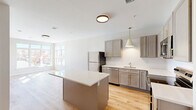 Located at 448 Waterman Ave in East Providence, RI, this thoughtfully designed one-bedroom, one-bathroom residence offers a clean, modern aesthetic across a single floor. Light-toned hardwood-style flooring runs throughout, lending warmth and continuity to every room.

The heart of the home is an open-concept living, dining, and kitchen area. The kitchen is well-appointed with gray shaker-style cabinetry accented by gold hardware, a white subway tile backsplash, quartz countertops, and a full suite of stainless steel appliances including a refrigerator, range, microwave, and dishwasher. A central island with a crisp white countertop provides additional prep space and casual seating. Pendant lighting with gold fixtures adds a refined touch overhead.

The living area benefits from large windows that invite abundant natural light. The bedroom is a comfortable, serene space featuring a large multi-pane window with views of the surrounding neighborhood, allowing natural light to fill the room throughout the day.

The bathroom includes a full tub-shower combination and overhead cabinetry for added storage. Additional conveniences include two closets, a dedicated laundry area, and a utility room, ensuring practical functionality throughout. The overall palette of soft whites and warm neutrals creates a bright, inviting ambiance.