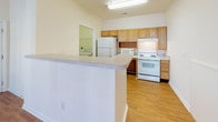 Located at 916 Sugar Gap Rd in Wake Forest, NC, this single-floor unit offers a thoughtfully designed layout with a blend of comfort and accessibility. The living area features rich hardwood-style flooring, a ceiling fan, and a large window that invites natural light and outdoor views, creating a bright and open atmosphere. A pendant light fixture highlights the transition between the living and dining areas, adding a touch of warmth to the open-concept flow.

The kitchen is equipped with oak-toned cabinetry, white appliances including a range, refrigerator, and built-in microwave, all set atop hardwood-style flooring. A wraparound peninsula provides additional counter space and serves as a natural divider between the kitchen and the main living area. A dedicated laundry space is conveniently accessible from the kitchen.

The bedrooms are carpeted for comfort, with generous windows offering outdoor views and ceiling fans for climate control. The primary bedroom includes direct access to a walk-in closet and an en-suite bathroom. Bathrooms throughout the unit are designed with accessibility in mind, featuring grab bars, an open vanity with knee clearance, and a tub-shower combination with safety rails — making this unit well-suited for a range of mobility needs.