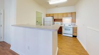 Located at 916 Sugar Gap Rd in Wake Forest, NC, this single-floor unit offers a thoughtfully designed layout with a blend of comfort and accessibility. The living area features rich hardwood-style flooring, a ceiling fan, and a large window that invites natural light and outdoor views, creating a bright and open atmosphere. A pendant light fixture highlights the transition between the living and dining areas, adding a touch of warmth to the open-concept flow.

The kitchen is equipped with oak-toned cabinetry, white appliances including a range, refrigerator, and built-in microwave, all set atop hardwood-style flooring. A wraparound peninsula provides additional counter space and serves as a natural divider between the kitchen and the main living area. A dedicated laundry space is conveniently accessible from the kitchen.

The bedrooms are carpeted for comfort, with generous windows offering outdoor views and ceiling fans for climate control. The primary bedroom includes direct access to a walk-in closet and an en-suite bathroom. Bathrooms throughout the unit are designed with accessibility in mind, featuring grab bars, an open vanity with knee clearance, and a tub-shower combination with safety rails — making this unit well-suited for a range of mobility needs.