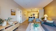This thoughtfully designed single-floor residence offers a seamless open-concept layout that connects the living, dining, and kitchen areas into one cohesive, functional space. Light-toned luxury vinyl plank flooring runs throughout the main areas, creating a clean and consistent foundation that enhances the sense of openness.

The kitchen is a standout feature, outfitted with crisp white shaker cabinets, a classic white subway tile backsplash, quartz countertops, and stainless steel appliances including a range, microwave, and refrigerator. Under-cabinet lighting adds both practicality and ambiance, while pendant lights above the kitchen island provide an elegant finishing touch.

The living area offers a welcoming and comfortable atmosphere, anchored by cool-toned walls and tasteful décor. Natural light filters in through well-placed windows, complementing the warm artificial lighting throughout. A dedicated seating area provides an inviting setting for relaxation.

The bedroom is a calm retreat, featuring plush carpeting, a large window with outdoor views of surrounding greenery, and soft neutral tones. A generously sized walk-in closet with wire shelving systems offers ample storage.

The bathroom is finished with a white shaker-style vanity, quartz countertop, undermount sink, and brushed nickel fixtures, maintaining the clean, modern aesthetic found throughout the entire residence.