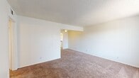 This 2-bedroom, 2-bathroom unit is laid out entirely on a single floor, making it easy to navigate. The living room features warm neutral-toned carpet, a textured ceiling, and a large window that allows natural light to fill the space, with a direct sightline toward the kitchen. The kitchen is equipped with white cabinetry, a double-basin stainless steel sink, speckled blue-gray countertops, and a white range and refrigerator — providing all essential cooking amenities in a clean, functional arrangement. A hallway connects the main living areas to the two bedrooms and bathrooms. Both bedrooms are carpeted in the same warm tone as the living room, featuring neutral white walls and a quiet, understated ambiance well-suited for restful use. The primary bedroom is a comfortable size, while the second bedroom offers a cozy alternative. One bathroom features full white square tile surrounding a soaking tub with an operable window above, providing ventilation and natural light. The second bathroom area includes a vanity with white cabinetry, a speckled countertop, and a large mirror. The entry area transitions from wood-look flooring to carpet and benefits from a large side window. Overall, the unit presents a clean, functional, and move-in-ready layout.