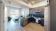 Located at 201 The Promenade N in Long Beach, California, this modern one-bedroom, one-bathroom unit offers a thoughtfully designed open-concept layout. The kitchen is a standout feature, showcasing rich dark wood cabinetry, deep teal subway tile backsplash, stainless steel appliances including a gas range, built-in microwave, side-by-side refrigerator, dishwasher, and a wine cooler. Pendant lighting over the kitchen peninsula adds warmth, while the space flows seamlessly into the living area, which benefits from natural light through sliding glass doors. Exposed concrete ceilings and industrial ductwork lend an urban loft character throughout the unit, complemented by warm hardwood-style flooring. The bedroom is a comfortable retreat featuring large windows that frame outdoor views of the surrounding neighborhood, along with direct access to a well-organized closet. The bathroom is finished with bold hexagonal tile flooring and clean white walls, creating a modern and polished aesthetic. A dedicated closet provides practical storage. This unit combines industrial-chic design elements with modern finishes, making it an appealing urban residence in the heart of Long Beach's vibrant Promenade district.
