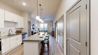 This thoughtfully designed 1-bedroom, 2-bathroom residence offers an efficient and stylish single-floor layout. The open-concept living, dining, and kitchen area serves as the heart of the home, featuring light wood-style flooring that flows seamlessly throughout. The kitchen is outfitted with crisp white shaker cabinets, a white subway tile backsplash, stainless steel appliances, and a large granite-topped island with bar seating — illuminated by a trio of globe pendant lights. The living room benefits from multiple windows that bring in generous natural light and outdoor views, complemented by a ceiling fan overhead. The primary bedroom is a comfortable retreat with tall ceilings, natural light from dual windows, and direct access to one of the two bathrooms. The en-suite bathroom features a granite double-vanity with white cabinetry, a soaking tub, and a walk-in shower. A second bathroom provides additional convenience for guests. Storage is well-addressed with two closets — including a spacious walk-in fitted with wire shelving — alongside a pantry, laundry area, and a dedicated utility room. Neutral wall tones and consistent finishes create a cohesive, modern ambiance throughout.