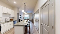 This thoughtfully designed 1-bedroom, 2-bathroom residence offers an efficient and stylish single-floor layout. The open-concept living, dining, and kitchen area serves as the heart of the home, featuring light wood-style flooring that flows seamlessly throughout. The kitchen is outfitted with crisp white shaker cabinets, a white subway tile backsplash, stainless steel appliances, and a large granite-topped island with bar seating — illuminated by a trio of globe pendant lights. The living room benefits from multiple windows that bring in generous natural light and outdoor views, complemented by a ceiling fan overhead. The primary bedroom is a comfortable retreat with tall ceilings, natural light from dual windows, and direct access to one of the two bathrooms. The en-suite bathroom features a granite double-vanity with white cabinetry, a soaking tub, and a walk-in shower. A second bathroom provides additional convenience for guests. Storage is well-addressed with two closets — including a spacious walk-in fitted with wire shelving — alongside a pantry, laundry area, and a dedicated utility room. Neutral wall tones and consistent finishes create a cohesive, modern ambiance throughout.