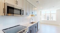 Located at 2105 Bond St in Charlottesville, VA, this efficiently designed single-floor unit offers a thoughtfully planned layout comprising a living room, kitchen, bathroom, and closet. Light hardwood flooring runs throughout the main living areas, contributing to a clean, contemporary aesthetic.

The kitchen is a standout feature, showcasing two-tone cabinetry with gray lower cabinets and white upper cabinets, accented by sleek matte black hardware. Quartz countertops, a classic white subway tile backsplash, a stainless steel under-mount sink, and stainless steel appliances — including an electric range, over-the-range microwave, refrigerator, and dishwasher — complete the space with a polished, modern finish.

The living area is bright and airy, benefiting from large multi-pane windows that invite abundant natural light and offer views of the surrounding neighborhood. The open layout provides a versatile space for both lounging and dining.

The bathroom features large-format tile walls in a neutral stone tone, a glass-enclosed walk-in shower with a built-in bench, and tile flooring, creating a spa-like atmosphere. A dedicated closet provides practical storage. The unit's clean lines, neutral palette, and modern finishes make it a well-appointed space in a contemporary residential community.