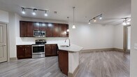 Located at 155 Birdsall St in Houston's 77007 zip code, this single-floor residence offers a well-appointed, open-concept layout designed for comfortable everyday living. The kitchen is a standout feature, showcasing rich dark wood cabinetry, granite countertops, and a full suite of stainless steel appliances including a range, microwave, and bottom-freezer refrigerator. A peninsula with an undermount sink and pendant lighting above creates a natural gathering point that connects the kitchen to the open living area. Wood-look plank flooring runs throughout the main living spaces, providing a clean, cohesive aesthetic accented by track lighting overhead. The bedroom is generously sized, finished with plush carpet, a ceiling fan, and direct access to both a spacious walk-in closet outfitted with wire shelving and a private en-suite bathroom. The bathroom features large-format tile flooring, a dual-sink vanity with granite countertops and dark wood cabinetry, a framed mirror, and a glass-enclosed shower. In-unit laundry hookups add everyday convenience. The neutral color palette and clean finishes throughout lend the space a move-in-ready, modern feel.