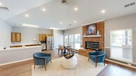Located at 4900 Chandler Ridge Circle in Raleigh, NC, this single-story space offers a well-organized layout across a generously sized floor plan. The living and kitchen area serves as the heart of the space, highlighted by a striking full-height brick fireplace flanked by large windows that flood the room with natural light. The vaulted ceiling adds a sense of openness, while warm hardwood flooring flows consistently throughout. The kitchen features warm-toned wood cabinetry, white countertops, stainless steel appliances including a French door refrigerator and dishwasher, and a peninsula that defines the transition between kitchen and living areas. The hallway entry provides a bright, welcoming reception area with a ceiling fan, multiple windows, seating, and direct exterior access. An adjacent workspace area features recessed lighting beneath a vaulted ceiling and provides ample room for workstations and seating. The dedicated exercise room is equipped with fitness equipment, motivational wall décor, crown molding, a ceiling fan, and its own exterior door. Together, these rooms create a functional, well-lit, and thoughtfully arranged space suited for a variety of uses.