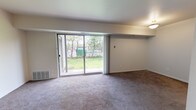 This single-story unit in Ypsilanti, Michigan, offers a practical and functional layout designed to maximize the use of its available space. The living area is carpeted and features a large sliding glass door that opens to an outdoor view of greenery, allowing natural light to fill the room. A floor-level vent provides climate control, and the neutral wall tones create a clean, understated atmosphere throughout.

The galley-style kitchen runs along two parallel walls, featuring warm wood-toned cabinetry on both upper and lower sections, light countertops, a stainless steel sink, and white appliances including a stovetop range and refrigerator. Durable tile-pattern flooring grounds the space practically.

The bedroom is generously proportioned with plush carpeting and a window that brings in natural light. A standout feature is the dual closet configuration — two side-by-side bifold-door closets, one offering hanging space and the other providing built-in shelving, delivering ample storage options.

The full bathroom includes a tiled tub-shower combination with chrome fixtures, a vanity with mirror, and tile-pattern flooring that complements the overall neutral palette. Throughout the unit, the consistent use of light walls and carpet contributes to a cohesive, easy-to-personalize living environment.