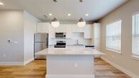 Located at 7551 Narcoossee Rd in Orlando, FL, this well-designed one-bedroom, one-bathroom unit offers a thoughtfully planned layout with modern finishes throughout. Light-toned hardwood-style flooring flows continuously across the entire space, creating a cohesive and clean aesthetic.

The kitchen serves as the focal point of the unit, showcasing a large granite-topped island illuminated by two globe pendant lights. White shaker-style cabinetry reaches toward the ceiling, complemented by a white subway tile backsplash and stainless steel appliances, including a refrigerator, electric range, microwave, and dishwasher. Natural light enters through a window adjacent to the kitchen, brightening the space.

A sliding barn door leads from the main living area toward the bedroom, adding a contemporary architectural detail. The bedroom features warm neutral wall tones, a ceiling fan, and built-in open shelving for added storage, with direct access to a walk-in closet outfitted with wire shelving systems.

The bathroom is finished with large-format neutral tiles lining the tub surround, recessed dual niche shelving, and brushed bronze fixtures, delivering a clean and modern aesthetic. Recessed lighting throughout the unit ensures consistent, well-distributed illumination in every room.