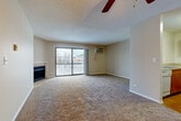 Located at 1589 Fairway Dr in Naperville, IL, this 2-bedroom, 2-bathroom residence offers a practical and comfortable single-floor layout. The open living room is a standout space, featuring plush wall-to-wall carpeting, a tile-surround fireplace, a ceiling fan, and a sliding glass door that opens onto a private balcony with outdoor views — filling the room with natural light. A wall-mounted AC unit provides additional climate control. The kitchen is positioned just off the living area and features wood cabinetry, hardwood-style flooring, and white appliances including a refrigerator, range, and built-in microwave. Both bathrooms are finished consistently, each offering a tub-shower combination with white tile surround, a wood-toned vanity with white countertop, a large mirror with overhead lighting, and hardwood-style flooring. The bedrooms are carpeted and well-sized; the primary bedroom includes a dedicated closet and natural light from a window. The second bedroom also features carpeting, a window, and a wall-mounted AC unit. Textured ceilings are found throughout the home, adding a classic touch to the overall design of this well-organized Naperville residence.