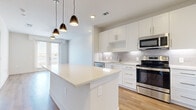 Located at 9877 W Valley Ranch Pkwy in Irving, TX, this well-designed one-bedroom, one-bathroom unit offers a clean, modern aesthetic across its single floor. The open-concept kitchen and living area serves as the heart of the space, anchored by a large central island with a quartz countertop and stylish pendant lighting overhead. The kitchen is outfitted with white shaker cabinetry, a subway tile backsplash, and a full suite of stainless steel appliances, including a refrigerator, range, microwave, and dishwasher. Light wood-tone flooring runs throughout the main living area, enhancing the bright and airy atmosphere. French doors in the living area allow natural light to pour in and provide access to an outdoor balcony with views of the surrounding neighborhood. The bedroom is a comfortable retreat featuring plush carpeting, a ceiling fan, and a window with neighborhood views. A dedicated walk-in closet off the bedroom offers built-in shelving and hanging rods for ample storage. The bathroom is finished with a white vanity, quartz countertop, framed mirror, and a combination tub and shower with marble-style tile surround, all tied together by matching wood-tone flooring.
