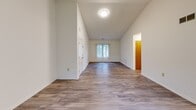 Located at 83 Fairway Ct in Lakewood, NJ, this single-floor, one-bedroom, one-bathroom home offers a well-designed layout with comfortable living spaces throughout. The open living and dining area immediately impresses with dramatic vaulted ceilings that amplify the sense of space, while wood-look plank flooring flows consistently underfoot. Large windows dressed with vertical blinds invite generous natural light and offer pleasant views of surrounding greenery, with a sliding glass door providing access to the outdoors. The kitchen is thoughtfully appointed with warm-toned wood cabinetry, a white countertop peninsula that doubles as a breakfast bar, and black appliances including a gas range and full-size refrigerator. A hallway connects the main living area to the private quarters of the home. The spacious primary bedroom is well-lit by multiple windows, continuing the wood-look flooring and maintaining the home's clean, neutral palette. Two closets provide ample storage, including a walk-in closet outfitted with wire shelving. The bathroom features a full tub-shower combo with white tile surround, a wide vanity with a mirror, and mosaic tile flooring. A dedicated hallway ties the layout together efficiently, completing this move-in-ready home.