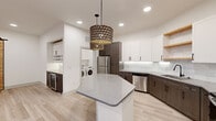 Located in Dallas's vibrant Ninth Street corridor, this thoughtfully designed single-floor residence combines contemporary aesthetics with practical functionality. The kitchen serves as the centerpiece of the home, showcasing an octagonal quartz-topped island beneath a pair of striking geometric pendant lights. Two-tone cabinetry — crisp white uppers paired with rich dark wood lowers — frames stainless steel appliances, open wood shelving, and a clean subway tile backsplash. Adjacent to the kitchen, a dedicated built-in bar area features under-cabinet lighting, a wine refrigerator, a built-in wine rack, and matching cabinetry, making it an ideal space for entertaining. Light wood-look flooring runs seamlessly throughout, lending warmth and continuity to the open layout. The bedrooms are bright and airy, each equipped with ceiling fans and French doors that open to outdoor views, filling the rooms with natural light. A sliding barn door adds a rustic-modern accent to one of the rooms. The bathroom is finished with bold geometric accent wallpaper, a gold-framed round mirror, and a tiled tub surround with black hardware accents. A walk-in closet with built-in shelving and rod storage provides generous organization space. In-unit Whirlpool washer and dryer complete this well-appointed home.