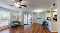 This single-floor residence offers a thoughtfully designed layout that balances comfort and functionality throughout. Rich, warm-toned hardwood flooring flows through the main living areas, complemented by neutral gray walls and textured ceilings with ceiling fans in each room for year-round comfort. The open living area is bright and welcoming, anchored by a sliding glass door that leads to a private patio overlooking lush, tropical greenery — allowing natural light to fill the space. A dedicated dining area with bar seating transitions seamlessly into the kitchen, which is equipped with stainless steel appliances, a mosaic tile backsplash, white cabinetry, and granite countertops that lend an elevated feel. Conveniently positioned adjacent to the kitchen is an in-unit laundry area with a full-size washer and dryer. The bedrooms provide a comfortable retreat — one features hardwood flooring and dual window access, while another is finished with plush carpeting and a ceiling fan, offering a softer, quieter atmosphere. The bathroom is well-appointed with a granite-topped vanity, white cabinetry, a full soaking tub with shower, and a large mirror that enhances the sense of space. Together, the rooms create a cohesive, move-in-ready environment with practical amenities throughout.