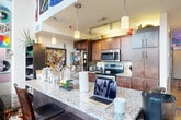 Located on Louise Ave in Charlotte's 28205 zip code, this two-story residence blends industrial character with eclectic personality across two thoughtfully arranged floors. The main level offers a generous living area anchored by soaring ceilings, exposed brick walls, and tall windows that draw in abundant natural light. Warm hardwood flooring runs throughout, complementing the raw, loft-inspired aesthetic. A dramatic floor-to-ceiling vinyl record display wall serves as a striking focal point in the main living space, adding vibrant color and artistic flair. The upper floor houses the private bedroom, featuring a wood-beamed ceiling with exposed structural elements, hardwood floors, and horizontal clerestory windows that provide light while maintaining privacy. A ceiling fan adds comfort to the cozy retreat. A second living area on this level functions as a media and lounge space, complete with hardwood floors and ample room for relaxation. Three full bathrooms are distributed across both floors, each featuring tile flooring, shower-tub combinations or walk-in showers, granite-topped vanities, and clean, neutral finishes. A staircase connects the two levels seamlessly. This distinctive Charlotte residence offers a compelling combination of industrial architecture, warm natural materials, and expressive living spaces.