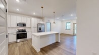 Located at 20 Graf Dairy Dr in Mobile, AL, this well-appointed single-story home offers 2 bedrooms and 2 bathrooms with a clean, modern aesthetic carried consistently throughout. The kitchen serves as a standout centerpiece, featuring a large island with a white quartz countertop and warm wood-toned cabinetry, complemented by full-height white upper cabinets, a herringbone tile backsplash, stainless steel appliances, and stylish pendant lighting. Light-toned hardwood-style flooring flows through the main living and kitchen areas, adding warmth and continuity. Both bedrooms are carpeted and receive generous natural light through multiple windows fitted with blinds, and each is equipped with a ceiling fan. The spacious primary bedroom connects to an en-suite bathroom featuring a double vanity with quartz countertops, wood-toned cabinetry, matte black fixtures, a framed mirror, and a glass-enclosed shower. The second bathroom mirrors this refined design with a single vanity and a combination tub/shower. Two closets provide ample storage, including a walk-in closet with wire shelving. The home's bright white walls, recessed lighting, and cohesive modern finishes create a fresh, move-in-ready atmosphere throughout.
