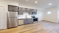 Located at 1245 N Anchor Way in Portland, Oregon, this well-designed one-bedroom, one-bathroom unit offers a thoughtful layout across a single floor. Light wood-tone flooring runs throughout, creating a warm, cohesive feel that ties each room together.

The galley-style kitchen is a standout feature, outfitted with sleek gray cabinetry, white quartz countertops, a full suite of stainless steel appliances including a refrigerator, electric range, built-in microwave, and dishwasher, and a modern sink with a gooseneck faucet. Recessed lighting and a clean white backsplash complete the polished look.

The living area flows naturally from the kitchen, with a charming porthole-style window and additional windows that invite natural light into the space. The bedroom is notably bright and airy, featuring soaring ceilings and a large floor-to-ceiling window that frames views of the surrounding Portland neighborhood. A dedicated closet provides ample storage.

The bathroom is finished with gray cabinetry, white countertops, black hardware accents, and a full tub-shower combination. In-unit laundry adds a practical convenience. Clean white walls, recessed lighting, and modern finishes throughout give this unit a crisp, contemporary ambiance.