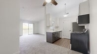 This single-floor, 2-bedroom, 1-bathroom residence offers a clean and modern layout designed for comfortable everyday living. The open-concept kitchen and living room serve as the heart of the home, with the kitchen showcasing white upper cabinetry, dark lower cabinets, stainless steel appliances including a refrigerator, range, and over-the-range microwave, and wood-look vinyl flooring. A pendant light fixture illuminates the space, which connects seamlessly to the carpeted living area via a pass-through window. The living room is generously sized, featuring a ceiling fan, neutral carpet, and sliding glass door access to a private balcony with outdoor views. Both bedrooms are carpeted and bathed in natural light through sliding windows that frame views of lush greenery. The primary bedroom includes a walk-in closet and convenient access to the full bathroom. The full bathroom features wood-look vinyl flooring, a dark vanity with a white countertop, and a tub-shower combination. A hallway connects the private quarters to the main living spaces, and the textured ceilings and bright white walls throughout contribute to the home's clean, cohesive aesthetic.