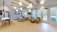 Located at 713 S Buncombe Rd in Greer, South Carolina, this single-story clubhouse serves as a contemporary community hub designed with a cohesive modern aesthetic throughout. Herringbone-patterned light wood flooring runs seamlessly across the entire space, anchoring the design and lending warmth to each area.

The main lounge is an open, generously scaled gathering space featuring exposed wood ceiling beams and oversized globe pendant lights that create a welcoming ambiance. A textured stone accent wall frames a mounted television, while large windows and glass doors flood the room with natural light and provide direct views of the outdoor pool area. Comfortable seating arrangements invite casual socializing.

Adjacent to the lounge, a dedicated dining area showcases a built-in cabinetry niche with a dark accent wall backdrop, adding depth and visual interest. The space connects to a glass-enclosed private office or conference room, offering functional versatility.

The leasing or business center features a striking quartz-topped island with waterfall veining, complemented by soft blue tile backsplash, warm wood cabinetry, open display shelving, and sleek pendant lighting. A sink and ample counter space complete this highly functional area. Throughout, the design balances contemporary style with practical amenities.