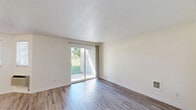 Located in Spokane Valley, WA, this single-floor 1-bedroom, 1-bathroom unit offers a clean, functional layout designed for comfortable everyday living. The living area features wood-style vinyl flooring, neutral white walls, and a textured ceiling, with a sliding glass door that fills the space with natural light and provides direct access to a green outdoor area. A hallway connects the main living spaces, transitioning from the open living area to the private quarters. The kitchen is efficiently arranged in an L-shape, equipped with white cabinetry featuring light wood trim, laminate countertops, a dishwasher, electric range, refrigerator, double sink, and a built-in desk area — all set on wood-style flooring with ceiling light fixtures. The bedroom offers plush carpeting, a baseboard heater, a window with natural light, and a closet for storage. The bathroom includes a green marbled vanity countertop with an undermount sink, a matching tub surround, wood-style flooring, a large mirror, and a toilet. A hallway with additional storage completes the layout. The unit presents a clean, move-in-ready aesthetic with a neutral color palette throughout.