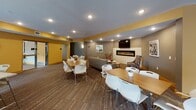 Located at 1301–1345 County Road D E in Maplewood, Minnesota, this single-floor community amenity space offers a thoughtfully designed collection of rooms built to support both social and active lifestyles. The central lobby serves as the heart of the space, featuring a dramatic double-height mezzanine level with bold yellow and gray accents, recessed lighting, a sleek linear fireplace, and curved stone-accented seating arrangements anchored by a geometric wood coffee table. Patterned carpeting and curated artwork add visual interest throughout.

Adjacent to the lobby, a spacious lounge area provides comfortable seating with a leather sofa and accent chairs, flowing into a community kitchen equipped with dark cabinetry, stainless steel appliances, granite countertops, a large island with bar seating, and pendant lighting above a window overlooking an outdoor area.

The fitness center is divided into two well-equipped sections: one featuring cardio machines including treadmills, ellipticals, and a stationary bike alongside wall-mounted TVs, and another dedicated to free weights, kettlebells, and exercise balls set against a bold teal accent wall.

A spirited game room rounds out the amenities, offering a full-size pool table, foosball, shuffleboard, and motivational artwork, creating a lively atmosphere for recreation and socializing.