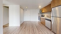 This contemporary 3-bedroom, 2-bathroom unit offers a thoughtfully designed single-floor layout that maximizes functionality and comfort. The open-concept living and kitchen area serves as the heart of the home, featuring light-toned hardwood-style flooring that flows seamlessly throughout. The kitchen is outfitted with warm wood cabinetry, a tiled backsplash, stainless steel appliances including a range, microwave, and dishwasher, complemented by a white refrigerator and a double sink. Track lighting adds a modern touch to the space.

The living area is bright and airy, with large sliding glass doors opening onto a private balcony that overlooks a natural, tree-lined landscape, allowing for abundant natural light. Two additional bedrooms also feature sliding door balcony access with similar outdoor views, while the third bedroom includes a built-in sliding closet. All bedrooms continue the consistent light hardwood flooring.

The two bathrooms are finished with large-format neutral floor tiles, wood-toned vanities with white countertops, and a full soaker tub surrounded by sleek subway tile. The unit also includes a dedicated laundry area. Clean white walls and a neutral palette throughout create a bright, modern ambiance well-suited for comfortable living.