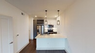 Located at 315 S Calhoun St in Fort Worth, TX, this single-floor unit showcases a thoughtfully designed, modern interior with a clean, contemporary aesthetic throughout. The open-concept kitchen is a standout feature, equipped with stainless steel appliances including a side-by-side refrigerator with water dispenser, electric range, and over-the-range microwave. White shaker cabinetry with a classic subway tile backsplash contrasts elegantly with dark lower cabinets and rich dark hardwood-style flooring. A generous white quartz peninsula with an undermount stainless steel sink and stylish industrial pendant lighting serves as the centerpiece, providing both workspace and casual dining potential. A built-in wine rack adds a refined touch to the kitchen area. The living space is bright and open, benefiting from natural light through windows fitted with blinds, and is complemented by additional pendant and flush-mount ceiling lighting. Crisp white walls throughout lend the space an airy, clean atmosphere. The bathroom is well-appointed with white subway tile surrounding a full soaking tub and shower combo, a dark gray vanity with a white countertop, matching overhead cabinetry, and light tile flooring, creating a polished, functional retreat.