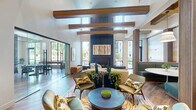 Located at 412 Summer St in Abington, Massachusetts, this thoughtfully designed single-floor community space offers a generous and versatile layout across its living area. The space makes a striking first impression with soaring vaulted ceilings accented by warm wood beams, wide-plank hardwood flooring, and an abundance of natural light streaming through expansive floor-to-ceiling windows and glass partitions.

The living area serves as the heart of the space, anchored by a dramatic floor-to-ceiling dark panel fireplace wall adorned with a vibrant art piece above the wide linear hearth. Comfortable seating arrangements on patterned area rugs invite relaxation, while the open sightlines connect seamlessly to adjacent zones.

A welcoming lounge area near the entrance features an eye-catching sculptural chandelier with golden leaf-like elements, eclectic upholstered seating, and curated artwork, flowing naturally into a reception area with a circular ceiling detail. A glass-partitioned game room houses multiple poker and gaming tables with sleek black chairs, centered around a bold teal mosaic wet bar with pendant globe lighting. Curated wall art and lush greenery add warmth and character throughout, creating a cohesive, sophisticated ambiance that balances modern design with comfortable, communal functionality.