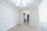 This single-floor residence offers a well-organized layout with a variety of functional spaces finished in a neutral, warm palette throughout. The main living and dining areas feature light ceramic tile flooring and are accented by crown molding and a decorative chandelier, lending a polished character to the open feel of the space. A chair rail detail runs along the walls, adding a subtle architectural touch.

The galley-style kitchen is equipped with rich cherry-toned cabinetry, dark granite-style countertops, and white appliances including a range, refrigerator, and built-in microwave. Tall ceilings in the kitchen enhance the sense of openness.

The bedrooms are carpeted and receive natural light through multiple windows fitted with blinds, offering views of the surrounding community's greenery. The arched panel interior doors are consistent throughout the unit, contributing to a cohesive design.

Two bathrooms are present, each featuring matching cherry vanities with dark countertops and tile flooring. One includes a tub/shower combination with a curved rod, while the second offers a walk-in shower with a safety grab bar.

A private balcony provides outdoor access with views of landscaped grounds and the broader residential community under open skies.