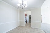 This single-floor residence offers a well-organized layout with a variety of functional spaces finished in a neutral, warm palette throughout. The main living and dining areas feature light ceramic tile flooring and are accented by crown molding and a decorative chandelier, lending a polished character to the open feel of the space. A chair rail detail runs along the walls, adding a subtle architectural touch.

The galley-style kitchen is equipped with rich cherry-toned cabinetry, dark granite-style countertops, and white appliances including a range, refrigerator, and built-in microwave. Tall ceilings in the kitchen enhance the sense of openness.

The bedrooms are carpeted and receive natural light through multiple windows fitted with blinds, offering views of the surrounding community's greenery. The arched panel interior doors are consistent throughout the unit, contributing to a cohesive design.

Two bathrooms are present, each featuring matching cherry vanities with dark countertops and tile flooring. One includes a tub/shower combination with a curved rod, while the second offers a walk-in shower with a safety grab bar.

A private balcony provides outdoor access with views of landscaped grounds and the broader residential community under open skies.