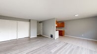 This single-floor unit offers a functional and well-organized layout across several distinct spaces. The open living and dining area is finished with light wood-style luxury vinyl flooring and neutral grey walls, creating a clean, understated aesthetic. A window overlooks greenery outside, allowing natural light to fill the room, while baseboard heating runs along the perimeter for climate control.

The galley-style kitchen is efficiently designed with warm wood cabinetry lining both walls, light granite-style countertops, and tile flooring. It is equipped with a gas range and white appliances, including a refrigerator and dishwasher, with ample upper and lower cabinet storage.

The bedrooms feature a mix of carpet and hard flooring, with windows framing outdoor greenery and wall-mounted air conditioning units supplementing the baseboard heating. Closet storage is present in the bedrooms.

Two bathrooms serve the unit. One features a tub-shower combination with white tile surround, a vanity with a mirrored medicine cabinet, and mosaic tile flooring. The second bathroom includes a glass-door stand-up shower, white subway tile walls, and a decorative mosaic tile floor, providing a clean, classic finish throughout.