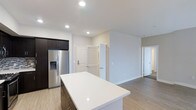 Located at 11921 Carmel Creek Road in San Diego, this single-story Plan B4 residence offers a thoughtfully designed open-concept layout that seamlessly connects the kitchen, dining, and living areas. The interior is finished with light-toned hardwood-style flooring throughout, contributing to a clean, cohesive aesthetic that enhances the sense of openness.

The kitchen is a standout feature, showcasing dark espresso cabinetry paired with a striking mosaic tile backsplash for contrast and visual interest. A large white countertop island anchors the space, providing generous prep and casual dining surface area. Stainless steel appliances, including a French door refrigerator and microwave, complete the modern culinary setup. Recessed lighting and a pendant track light fixture above the dining area ensure the space is well-lit throughout.

The open living and dining zone benefits from a neutral color palette of warm beige and white tones, creating a calm, inviting ambiance. A half-wall partition subtly defines spaces while maintaining visual flow. A bathroom is conveniently accessible from the main living area, and additional doors suggest dedicated bedroom and closet spaces. The overall design prioritizes functionality and contemporary style throughout.