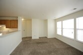 This single-floor residence offers a functional and straightforward layout designed for comfortable everyday living. The kitchen is arranged in a U-shaped configuration, outfitted with warm oak cabinetry offering generous upper and lower storage, light-toned countertops, and white appliances including a coil-top range, refrigerator, dishwasher, and double-basin sink. Tile flooring in a neutral stone pattern provides a durable, easy-to-clean surface throughout the kitchen area.

A half-wall peninsula separates the kitchen from the open living area, which flows seamlessly toward a dedicated entry door. The living space is finished with wall-to-wall carpet in a warm beige tone, creating a cohesive and comfortable atmosphere throughout the common areas and into the bedrooms. One bedroom benefits from a bank of windows along one wall plus an additional window, allowing notable natural light to fill the room. A second bedroom also features a window with blinds and offers a well-proportioned, versatile space.

The bathroom includes tile flooring, a full-size soaking tub with an overhead shower, chrome fixtures, and a vanity with countertop space. Clean white walls and neutral finishes throughout the unit contribute to a bright, move-in-ready aesthetic.