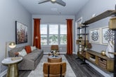 This single-floor residence is thoughtfully designed with a cohesive warm-neutral palette, combining hardwood-style flooring, soft carpet in the bedrooms, and grey-toned walls throughout. The living area is a standout space, featuring large windows dressed with rich rust-colored drapes that invite abundant natural light and outdoor views. A ceiling fan, open shelving unit, and carefully placed lighting fixtures contribute to the room's functional yet stylish character.

The kitchen is well-equipped with dark espresso cabinetry, granite countertops, stainless steel appliances including a refrigerator, range, and microwave, and a peninsula island with seating for casual dining. Pendant lighting overhead adds a refined touch to the space.

Both bedrooms are generously sized, each featuring plush carpeting, large windows with exterior views, and ample closet space. The primary bedroom connects directly to a well-appointed bathroom featuring a dual-sink vanity with granite countertops, dark cabinetry, a large mirror with vanity lighting, and hardwood-style flooring. A separate water closet provides added privacy. A walk-in closet is accessible from the bathroom, offering practical storage.