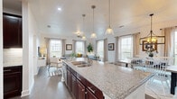 This well-appointed single-floor residence offers a thoughtfully designed layout that balances comfort and modern style. A clean, bright hallway with dark hardwood-style flooring and crisp white millwork serves as an elegant introduction to the home, with recessed lighting overhead and curated wall art adding a refined touch.

The heart of the home is the open-concept kitchen, dining, and living area. The kitchen features a generously sized center island with granite countertops, a double undermount sink, rich dark cabinetry, and pendant lighting overhead. It flows seamlessly into the living area, which is surrounded by multiple large windows that flood the space with natural light and offer pleasant outdoor views. The dining area is distinguished by a dramatic dark accent wall, gallery-style framing, and a statement lantern chandelier.

The primary bedroom is carpeted and warmly lit, providing a serene retreat with ample space. It connects to a private hallway that leads to a walk-in closet and a full bathroom featuring a tiled tub-shower combination, tile flooring, and a pedestal sink with a framed mirror. A secondary bedroom is equally inviting, with soft carpet, a large window, and a ceiling fan. An additional full bathroom offers a tiled tub-shower, natural window light, and clean neutral finishes throughout.