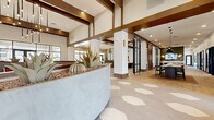 Located in Mesa, Arizona, this expansive single-floor clubhouse delivers a sophisticated blend of modern design and Southwest-inspired aesthetics. The grand entry lobby sets a striking tone with soaring ceilings, bold dark wood beam accents, and a signature geometric hexagonal tile floor that transitions seamlessly into warm wood-look flooring throughout the rest of the space. A curved reception desk anchors the lobby, flanked by a built-in desert succulent planter that adds a natural, organic touch reflective of the Arizona landscape.

The open living area is generously proportioned, bathed in natural light from floor-to-ceiling black-framed glass doors and windows that frame outdoor views. Thoughtfully curated seating arrangements — including a tufted banquette, lounge chairs, and café-style tables — create distinct yet connected social zones. Pendant lighting clusters in varied styles add warmth and visual interest overhead.

A dedicated mailroom and lounge area features a long communal table, stylish pendant fixtures, built-in mailboxes, and comfortable seating nooks. Co-working areas with glass-partitioned private pods and a shared worktable offer functional, professional spaces. Hallways connect each zone fluidly, maintaining the cohesive, upscale ambiance that defines this well-appointed community clubhouse.