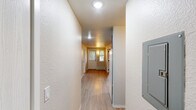 Located in the Roosevelt neighborhood of Seattle, WA, this efficient two-bedroom unit offers a practical, well-organized layout across a single floor. The entryway opens into a hallway finished with light-toned luxury vinyl plank flooring, which extends into the kitchen area. The kitchen is equipped with teal-blue cabinetry, a white refrigerator, and a range, providing a functional cooking space with a pop of color against the neutral walls.

Both bedrooms are carpeted in a neutral gray tone, offering a comfortable and quiet retreat. Each bedroom is served by baseboard heating, ensuring warmth during Seattle's cooler months. The primary bedroom features a sliding-door closet for efficient storage, while the second bedroom benefits from a window that brings in natural light and leafy outdoor views. A wall-mounted light fixture in the second bedroom adds a cozy, functional touch.

The unit maintains a consistent neutral color palette throughout — soft white and beige tones on the walls and ceilings — contributing to a clean, understated aesthetic. The textured ceilings and straightforward design keep the space feeling practical and easy to maintain. Overall, this unit offers a no-frills, functional living environment well-suited for those seeking a straightforward residence in a convenient Seattle location.