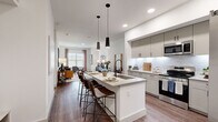 This thoughtfully designed 1-bedroom, 1-bathroom residence offers a comfortable and functional single-floor layout with modern finishes throughout. The open-concept living and dining area is bathed in natural light from large windows and features warm hardwood-style flooring that flows seamlessly across the main living spaces. The kitchen serves as a central hub, showcasing taupe shaker-style cabinetry, a white subway tile backsplash, stainless steel appliances including a refrigerator with ice maker, an electric range, and a built-in microwave. A central island with a sink, pendant lighting overhead, and bar seating makes it ideal for both cooking and casual dining. The living room provides a comfortable retreat with ample space for seating and a dining area. The bedroom is a serene space featuring a striking wood slat accent wall, dual windows, a ceiling fan, and direct access to the full bathroom. The bathroom is elegantly finished with large-format tile flooring, a dual-sink vanity with shaker cabinetry, quartz countertops, and a glass-enclosed shower with marble-style tile surround. The walk-in closet offers extensive built-in shelving and hanging space, and conveniently houses a stacked washer and dryer unit. A hallway connects the spaces efficiently, completing this well-organized and stylish residence.