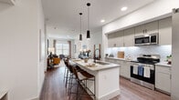 This thoughtfully designed 1-bedroom, 1-bathroom residence offers a comfortable and functional single-floor layout with modern finishes throughout. The open-concept living and dining area is bathed in natural light from large windows and features warm hardwood-style flooring that flows seamlessly across the main living spaces. The kitchen serves as a central hub, showcasing taupe shaker-style cabinetry, a white subway tile backsplash, stainless steel appliances including a refrigerator with ice maker, an electric range, and a built-in microwave. A central island with a sink, pendant lighting overhead, and bar seating makes it ideal for both cooking and casual dining. The living room provides a comfortable retreat with ample space for seating and a dining area. The bedroom is a serene space featuring a striking wood slat accent wall, dual windows, a ceiling fan, and direct access to the full bathroom. The bathroom is elegantly finished with large-format tile flooring, a dual-sink vanity with shaker cabinetry, quartz countertops, and a glass-enclosed shower with marble-style tile surround. The walk-in closet offers extensive built-in shelving and hanging space, and conveniently houses a stacked washer and dryer unit. A hallway connects the spaces efficiently, completing this well-organized and stylish residence.