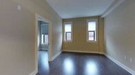 Unit 405 is a single-floor, 1-bedroom, 1-bathroom residence that offers a clean, functional layout with straightforward design elements. The main living area features dark hardwood-style flooring that runs throughout, providing a sleek contrast against the warm, neutral yellow-beige walls and crisp white trim and baseboards. Two windows along the primary wall allow natural light to filter into the space, offering views of the surrounding brick exterior streetscape. The room provides an open, unobstructed layout suitable for a variety of furniture arrangements.

A doorway leads directly into the bedroom, which continues the same flooring and color palette, maintaining a cohesive aesthetic throughout the unit. The bedroom also benefits from its own window, further enhancing natural light within the space. The consistent use of neutral tones and clean architectural lines gives the unit a simple, move-in-ready character. White window casings and door frames provide subtle contrast and definition to each room. Overall, Unit 405 presents a practical and well-maintained living space with a modest, understated design well-suited for everyday comfort.
