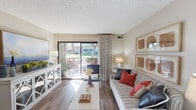 Located at 1690 Via Pacifica in Corona, California, this single-story residence offers a well-organized layout designed for comfortable everyday living. The living room serves as the heart of the home, featuring warm wood-style flooring, neutral-toned walls, and a textured ceiling. A large sliding glass door fills the space with natural light and opens directly onto an outdoor patio, providing views of surrounding greenery — a standout feature that enhances the room's open, airy feel. The dining area, positioned near the entryway, includes a ceiling fan and continues the wood-style flooring found throughout the main living spaces. The galley-style kitchen is efficiently arranged with white cabinetry, dark granite-style countertops, a double stainless steel sink, and black appliances including a refrigerator, electric range, and microwave. The bedroom is generously sized, finished with plush carpeting, and features a window overlooking the landscaped exterior. It connects directly to a private bathroom equipped with a full tub-and-shower combination. The overall aesthetic throughout the residence is warm and neutral, with consistent finishes that create a cohesive and inviting atmosphere from room to room.