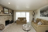This single-story home offers a well-organized layout designed for comfortable everyday living. The living room serves as a central gathering space, anchored by a full brick fireplace with a raised hearth and built-in shelving alongside it. Soft carpeting runs throughout, and a large sliding glass door floods the room with natural light while providing direct access to a private deck overlooking surrounding trees. Vertical blinds offer adjustable light control. The living area extends into a defined dining space, equipped with a ceiling fan and recessed lighting, which connects seamlessly to the brick fireplace wall, creating a cohesive open feel between the two areas.

The galley-style kitchen features rich dark cabinetry on both sides, offering generous storage. Tile flooring, a gas range, refrigerator, and a stainless steel sink with a dishwasher complete the functional space.

The primary bedroom is generously sized, with carpeted floors, a bright window, and the notable feature of two separate closets providing substantial storage. A second bedroom offers carpeted flooring and dedicated dresser space.

The bathroom includes a dark wood vanity with a wide countertop, an oversized mirror, and a three-bulb vanity light fixture, complemented by a separate shower area and louvered cabinet accents for a classic finish throughout.