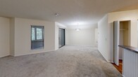This single-floor residence offers a practical and comfortable layout encompassing one bedroom, one bathroom, a combined kitchen and living room, a closet, and an in-unit laundry area. The open-concept living room is generously sized, featuring neutral-toned carpet, a textured ceiling, a pendant light fixture, and sliding glass doors alongside windows that invite natural light and outdoor views. A breakfast bar connects the living area to the kitchen, which is outfitted with warm honey-toned wood cabinetry, granite-style countertops, hardwood-style flooring, and black appliances including a range, built-in microwave, dishwasher, and refrigerator. The bedroom is a well-proportioned retreat with plush carpet, a ceiling fan with light kit, and a window with views of surrounding greenery. A reach-in closet provides convenient storage just off the main living space. The bathroom features a full soaking tub and shower combination with clean white surround and granite-style countertop accents. A dedicated laundry niche with a built-in utility shelf adds everyday convenience. Neutral warm-beige walls throughout create a cohesive and inviting atmosphere across the entire residence.