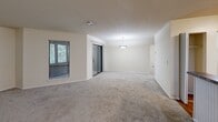 This single-floor residence offers a practical and comfortable layout encompassing one bedroom, one bathroom, a combined kitchen and living room, a closet, and an in-unit laundry area. The open-concept living room is generously sized, featuring neutral-toned carpet, a textured ceiling, a pendant light fixture, and sliding glass doors alongside windows that invite natural light and outdoor views. A breakfast bar connects the living area to the kitchen, which is outfitted with warm honey-toned wood cabinetry, granite-style countertops, hardwood-style flooring, and black appliances including a range, built-in microwave, dishwasher, and refrigerator. The bedroom is a well-proportioned retreat with plush carpet, a ceiling fan with light kit, and a window with views of surrounding greenery. A reach-in closet provides convenient storage just off the main living space. The bathroom features a full soaking tub and shower combination with clean white surround and granite-style countertop accents. A dedicated laundry niche with a built-in utility shelf adds everyday convenience. Neutral warm-beige walls throughout create a cohesive and inviting atmosphere across the entire residence.