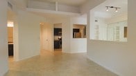 This single-floor residence features an open-concept design that seamlessly connects the living area to the kitchen. The space is finished with neutral-toned tile flooring throughout, contributing to a clean, cohesive aesthetic. Elevated ceilings with a structural beam detail add architectural interest and enhance the sense of vertical space.

The kitchen is outfitted with dark espresso cabinetry that provides a striking contrast against the light walls. Stainless steel appliances, including a refrigerator, stove, and microwave, are integrated into the layout. Granite or stone-look countertops complete the kitchen's functional and polished appearance. A pass-through window with a countertop overhang connects the kitchen to the adjacent living space, offering an open sightline and added versatility.

Built-in shelving is visible on one wall, providing practical storage or display space. The overall color palette is bright and neutral, with white walls and trim enhancing the natural light throughout. The layout flows efficiently, making the space feel open and well-organized. An interior door leads to additional areas of the unit, suggesting a thoughtful and functional floor plan.