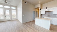 This contemporary single-floor unit showcases a clean, modern design with an open-concept layout that seamlessly connects the main living areas. Light-toned luxury vinyl plank flooring runs throughout the common spaces, complementing the neutral warm-beige walls and creating a bright, cohesive aesthetic.

The kitchen is a standout feature, boasting crisp white shaker cabinets with matte black hardware, light quartz countertops, a grey subway tile backsplash, and a full suite of stainless steel appliances including a refrigerator, electric range, and over-the-range microwave. A peninsula with pendant lighting provides additional prep space and casual seating.

The living area is exceptionally bright, featuring soaring ceilings, a ceiling fan, and a wall of oversized windows flanking French doors that open to a private balcony, flooding the room with natural light and outdoor views.

Bedrooms are finished with plush carpet and receive natural light through window placements. Bathrooms are well-equipped with white vanity cabinetry, quartz countertops, and tub-shower combinations. The primary bathroom connects to a dedicated walk-in closet with built-in shelving, adding practical storage. Recessed lighting throughout completes the polished, move-in-ready feel of this thoughtfully designed space.