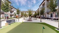 Located at 5173 Forest Lane Pl in Dallas, TX, this single-level outdoor courtyard amenity space is designed to foster community and recreation within a modern residential setting. The centerpiece of the space is a manicured putting green, complete with multiple flag holes, offering a leisure activity directly accessible from the plaza. A generously sized outdoor kitchen serves as a functional gathering hub, constructed with exposed brick bases topped with dark granite countertops. It is equipped with a stainless steel sink, a full-size stainless steel grill, and under-counter refrigeration units, making it well-suited for outdoor entertaining. A wood-beam pergola shelters the kitchen area, adding architectural character and partial shade. The open courtyard extends into a broad, light-colored concrete plaza flanked by neatly planted trees and manicured flower beds, with park-style benches inviting casual seating throughout. Overhead string lights are strung across the plaza, contributing to an inviting ambiance during evening hours. The surrounding multi-story brick and stucco buildings frame the space, creating an enclosed yet airy atmosphere. The overall design balances functionality with aesthetic appeal, integrating natural landscaping with durable, modern outdoor materials.